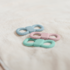 Strukturierte Silikon-Beißringe (Blau, Rosa, Mint) liegend auf weichem Untergrund, arrangiert als Set.