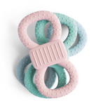 Drei übereinander gestapelte Beißringe in den Farben Rosa, Mint und Hellblau. Die Ringe haben eine 8er-Form mit Noppen-Struktur und einem geriffelten Mittelstück.